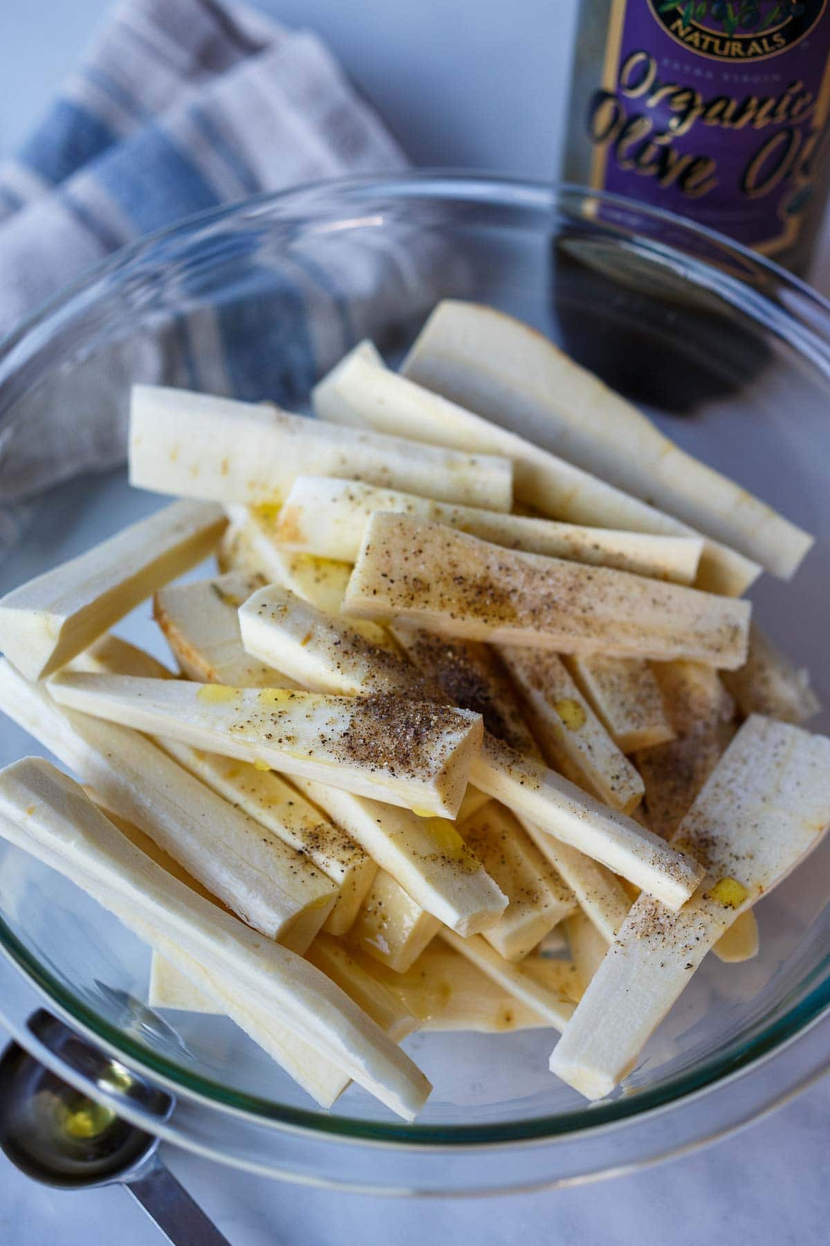 peeled parsnips in mixing bowl with oil, salt, pepper, and spices
