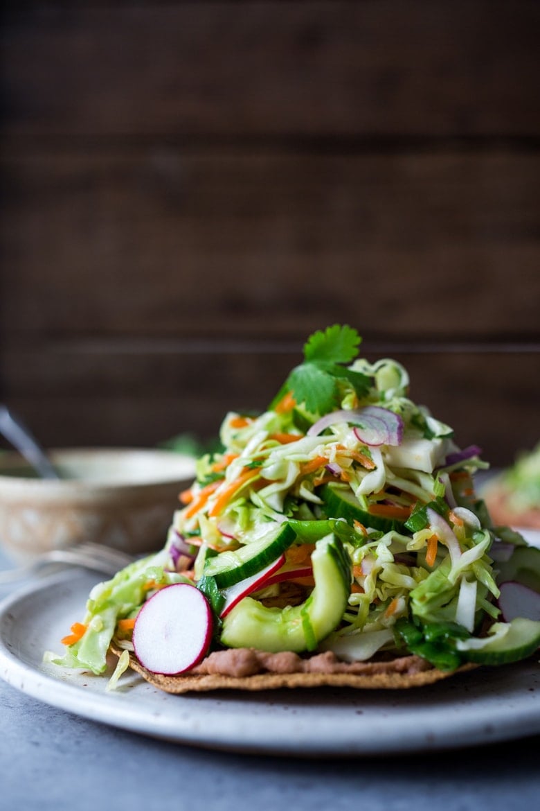 40 Mouthwatering Vegan Dinners!| Tlayudas Recipe! Traditional Oaxacan street food, tlayudas are a cross between a tostada and a pizza, made with a crispy tortilla, topped with refried beans, cheese (optional) cabbage slaw, avocado and cilantro. This healthy version is vegan and GF adaptable! | #tlayudas #tostadas #mexicanpizza #vegan #oaxacanfood #mexicanstreetfood #veganmexican #healthymexicanrecipes | www.feastingathome.com
