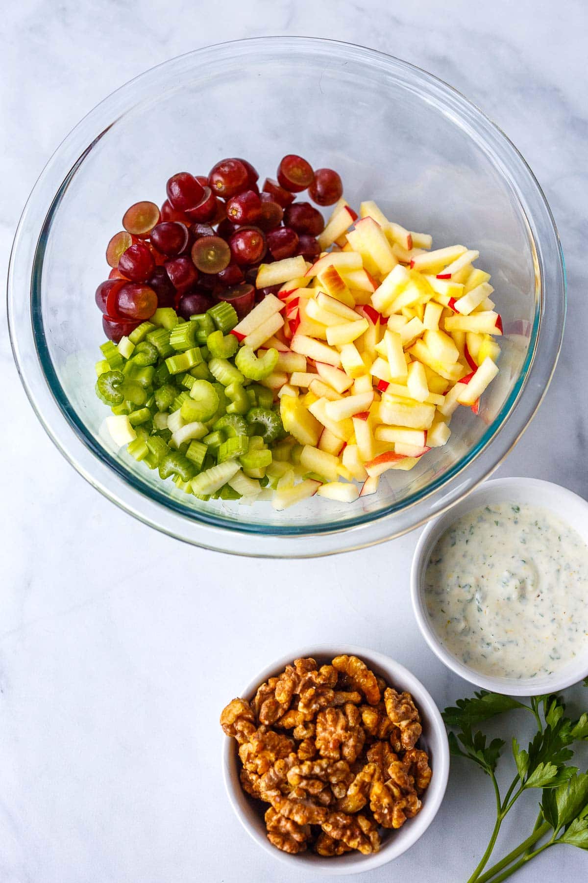 Waldorf Salad ingredients in a bowl with a seperate bowl of dressing and walnuts.